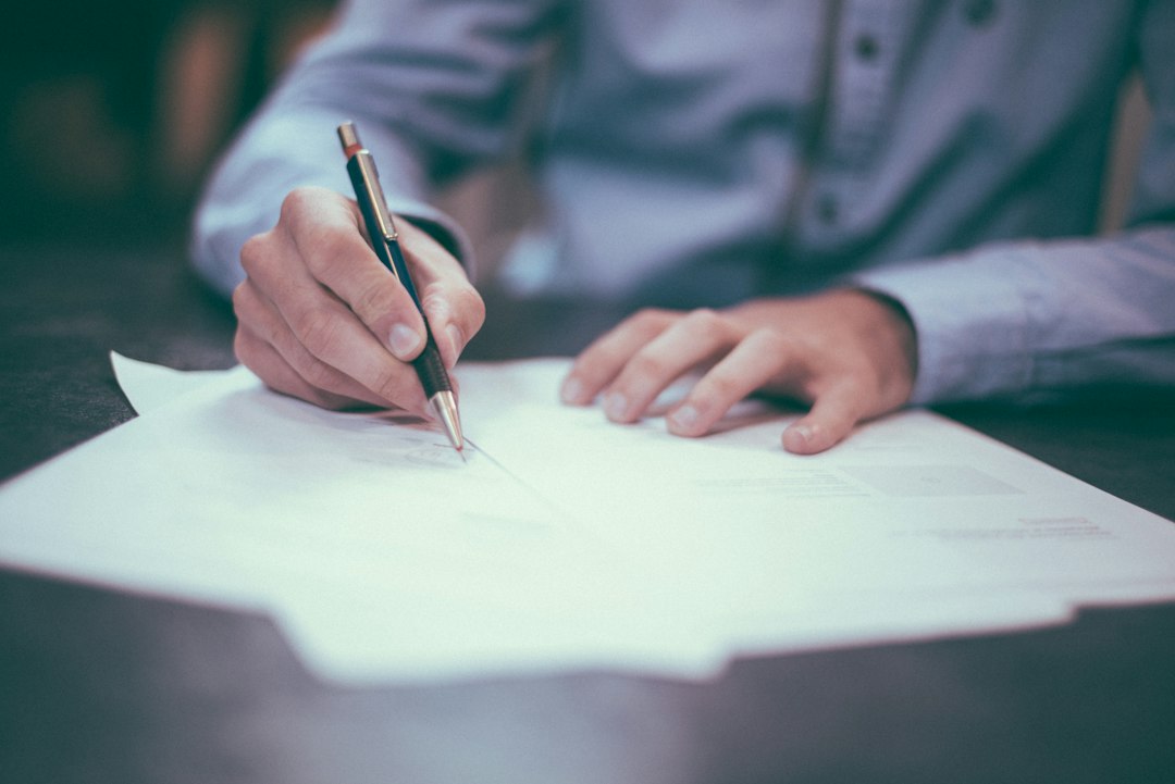 Hand signing a rental agreement on a desk with a pen