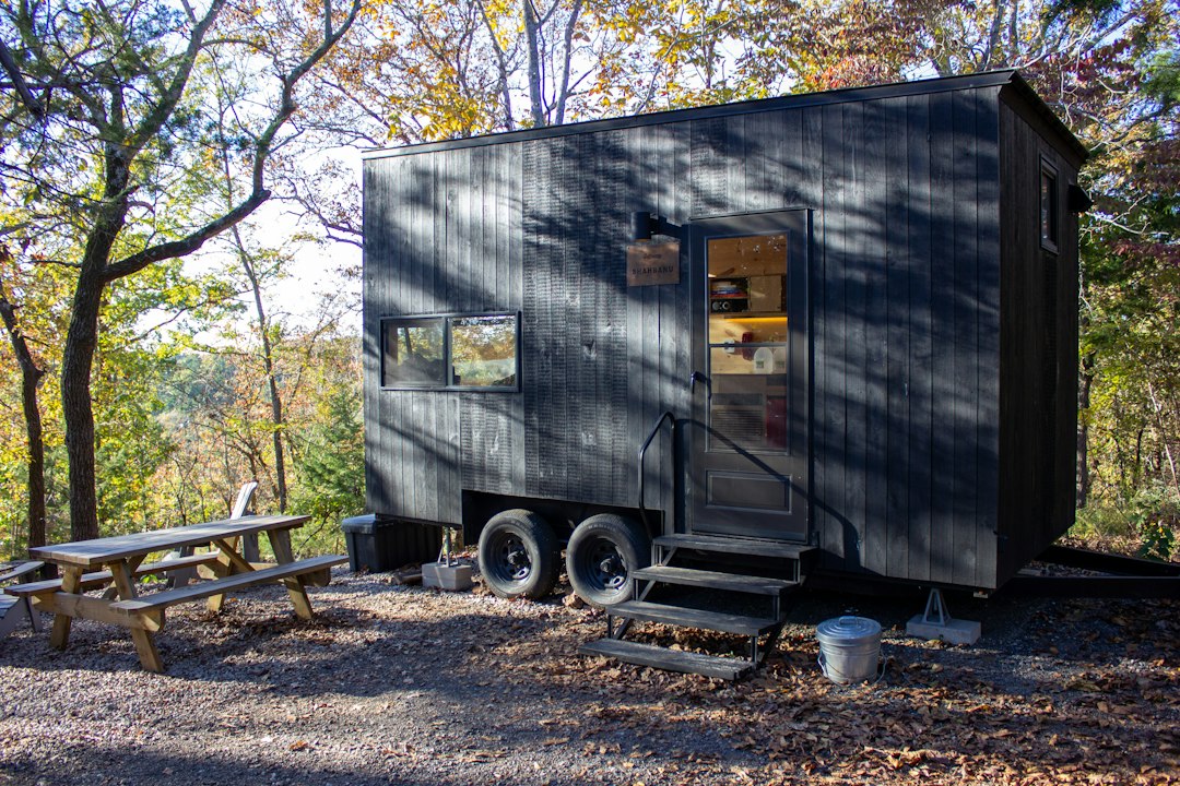 A tiny home on wheels with a picnic table outside, set among trees